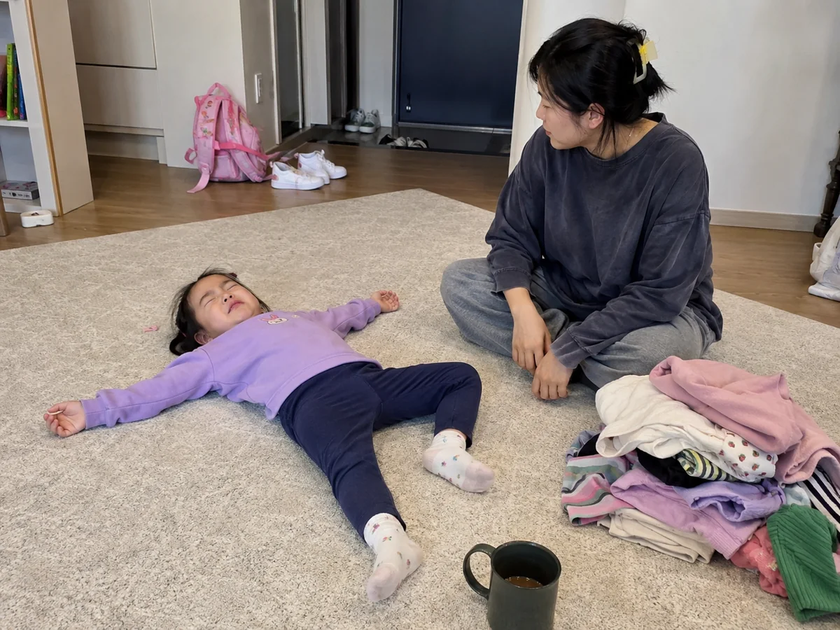 바닥에 누워 우는 아이 옆에 앉아 기다리는 엄마