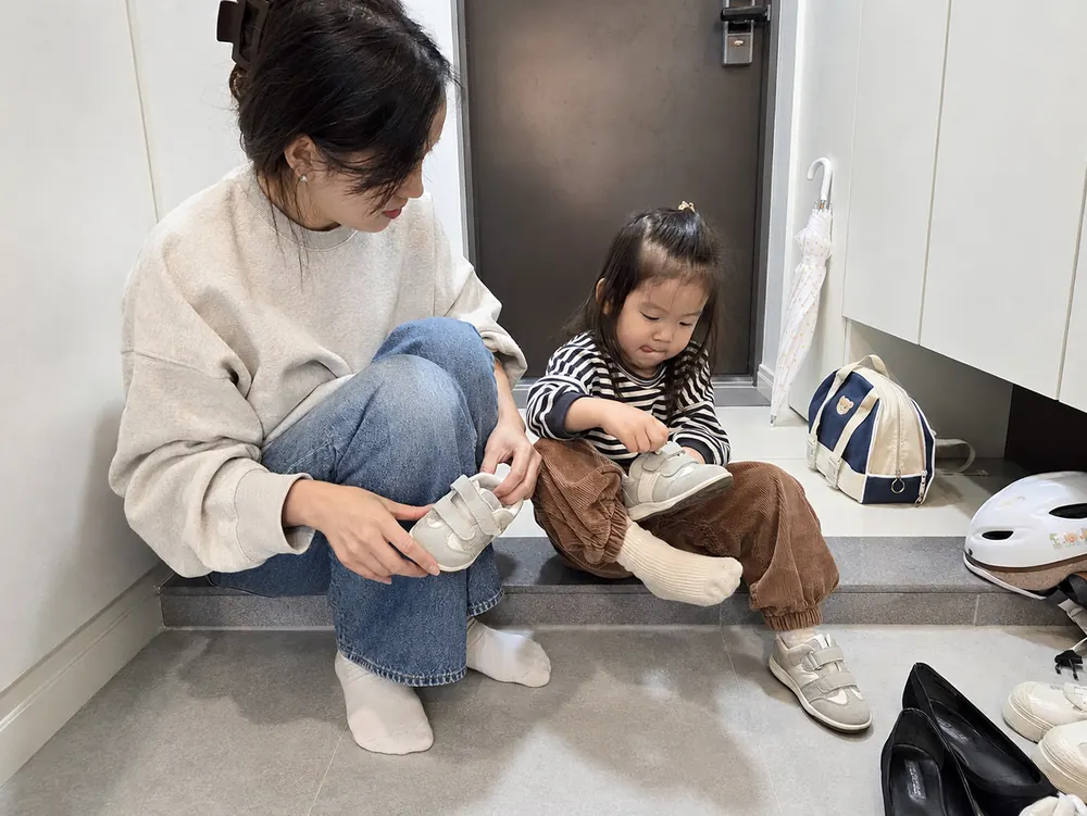 현관에서 스스로 신발을 신는 아이를 기다려주는 엄마