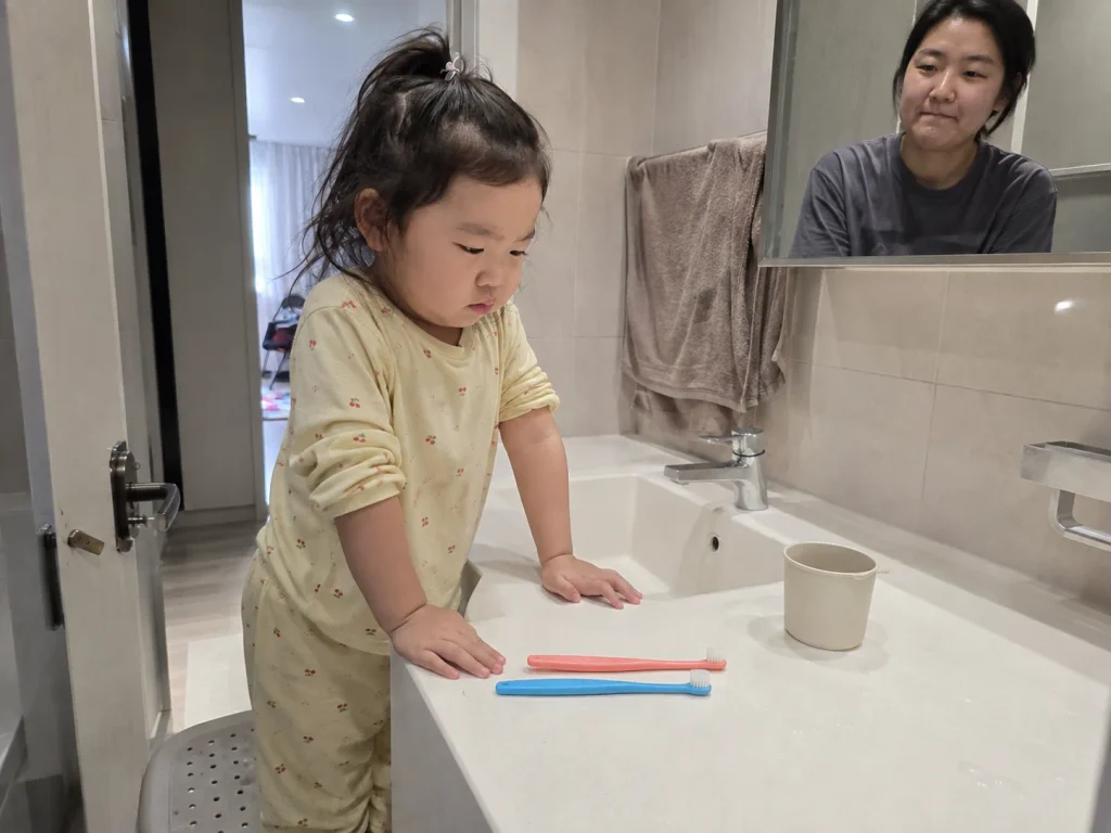 세면대 앞에서 두 개의 칫솔 중 하나를 고르는 아이