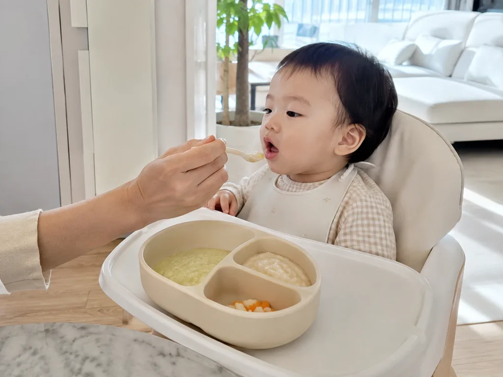 하이체어에 앉아 이유식을 받아먹는 아기