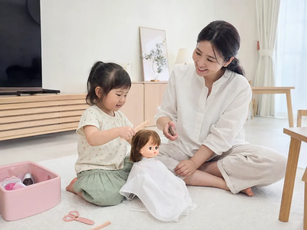 집에서 인형 머리를 빗으며 미용실 놀이를 하는 아이와 엄마
