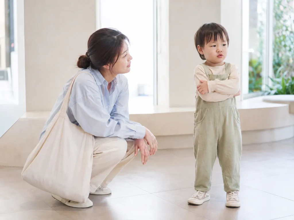 팔짱 낀 아이 앞에 쪼그려 앉아 차분히 기다리는 엄마