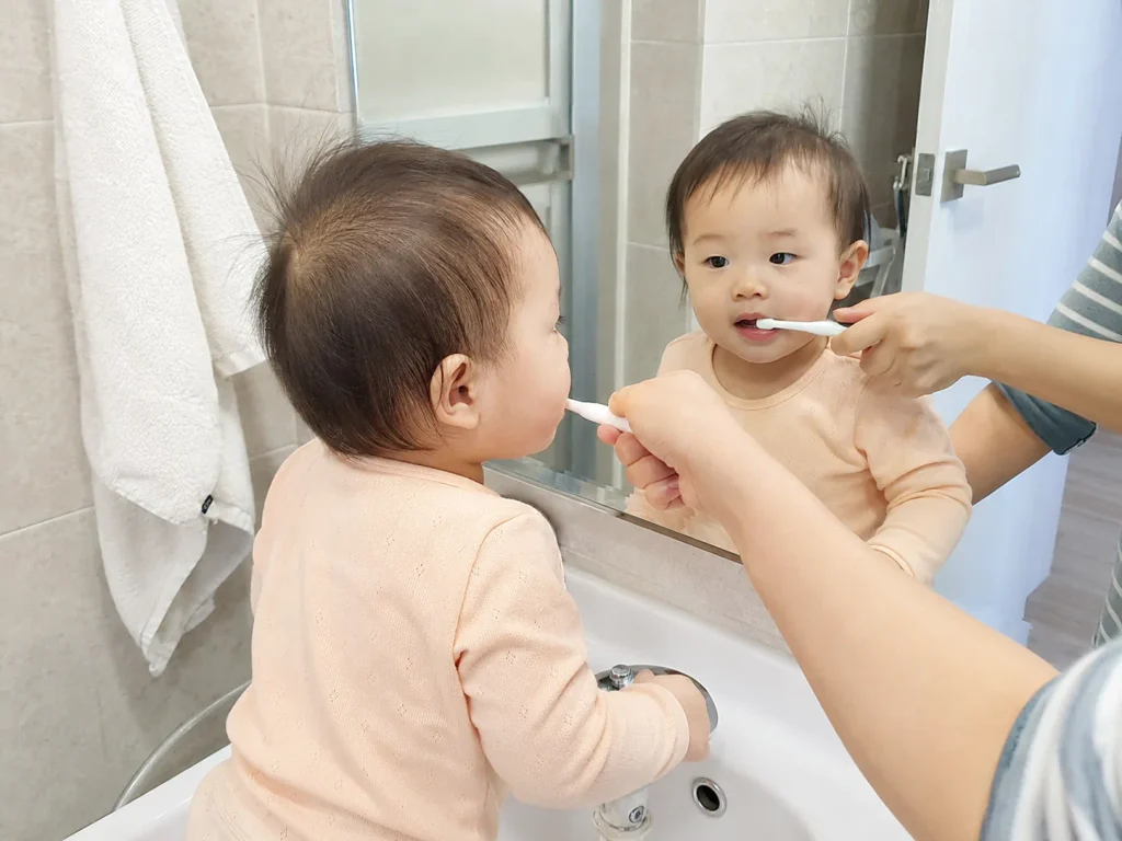 거울 앞에서 아기 첫니를 칫솔로 닦아주는 모습